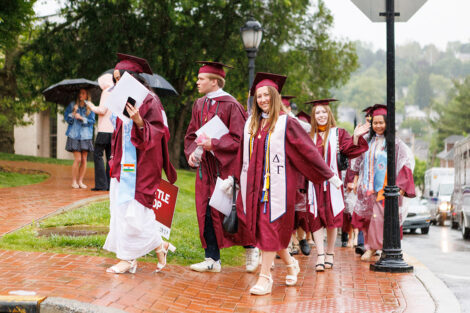Students walk in graduation gowns and a poncho.