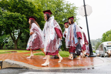 Students walk in graduation gowns and a poncho.