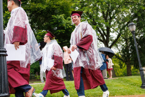 A student walks in their graduation gown and poncho.
