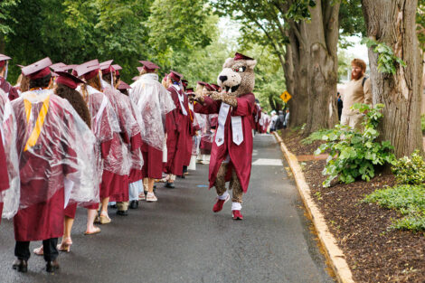 The Leopard, wearing a graduation cap and gown, points at graduates.