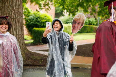 A family member takes a photo of their graduate, holding up a sign of their face.