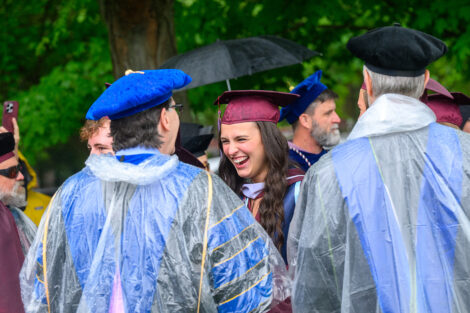 A graduate laughs as they talk with professors.