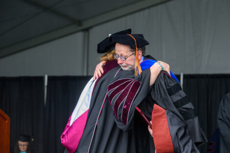 Audrey Flack's representative receives an honorary degree, embracing President Nicole Hurd.