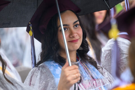 A graduate watches underneath an umbrella