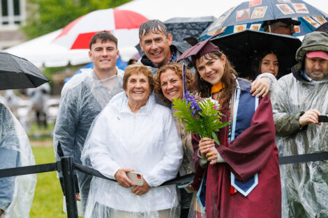 A graduate smiles, holding flowers and surrounded by family.