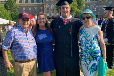 Four family members are standing on the Quad at Commencement. The graduate is wearing a cap and gown.