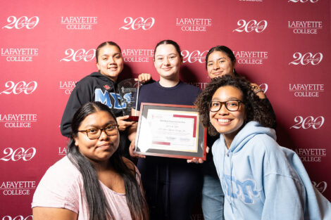 Members of Mu Sigma Upsilon Sorority Inc. are standing against a Lafayette maroon backdrop. One member is holding a framed award.