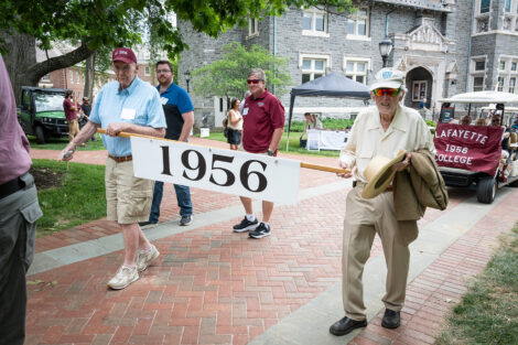 Two alumni from the Class of 1956 walk with a sign that reads 1956.