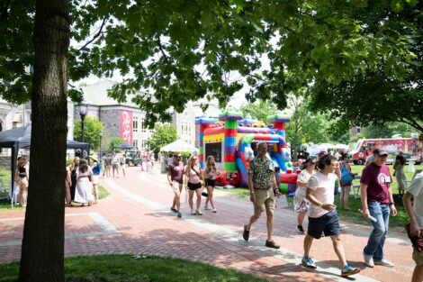 Alumni walk along the Quad path. A bouncy house and food trucks are in the background.