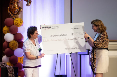 Ellen Kravet Burke '76 and President Nicole Hurd are standing on a stage holding a large white check.