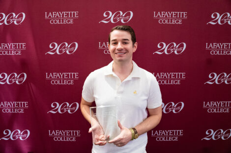 Daniel J.F. Lupia ’16 is standing and holding a glass award.