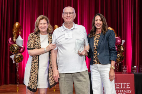 Jim Turner is standing on stage with President Hurd and Fran Della Badia. He is holding a glass award.