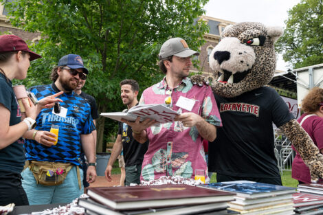 An alum is looking at a Melange yearbook. The Lafayette leopard mascot is looking over his shoulder.