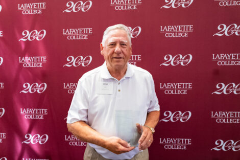 William Messick ’68 is standing and holding a glass award.