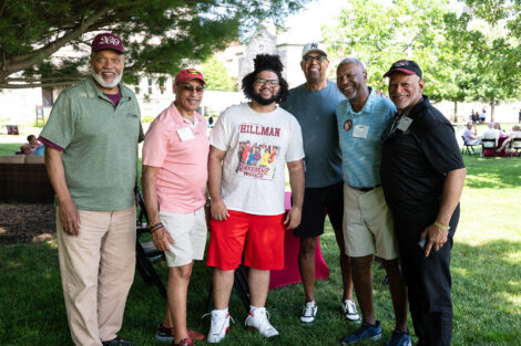 A group of six alumni stand on the Quad.