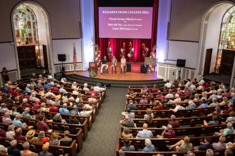 Top view of Colton Chapel. Three individuals are seated on a stage. There are balloons behind them.