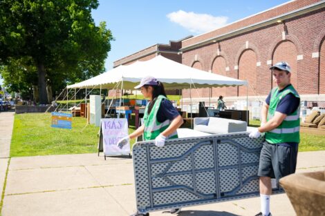 2 volunteers carry a folding table as they set up for West Ward Sale.