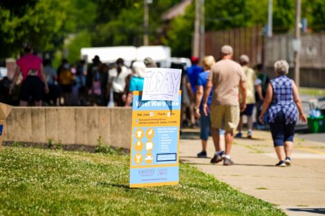 A yellow and blue sign advertising the West Ward Sale sits in the grass.