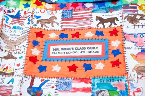A colorful quilt reads Mrs. Kolb's Class Quilt Palmer School 4th grade, with colorful quilt squares decorating the border.