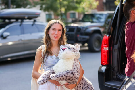 A student, carrying a stuffed Leopard, unloads a vehicle.