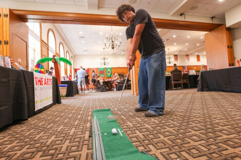 A student shows off golf skills in Marquis Hall where campus organizations were represented at tables in the background.