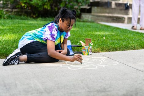 A student draws a chalk design on the sidewalk during ChalkFest.