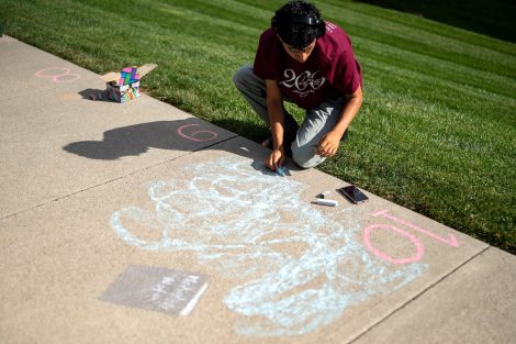 A student in a Bicentennial T-shirt draws a chalk design outside McKelvy House for ChalkFest.