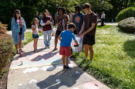 A young participant grabs chalk from a Lafayette student as he prepares to add his design at ChalkFest.